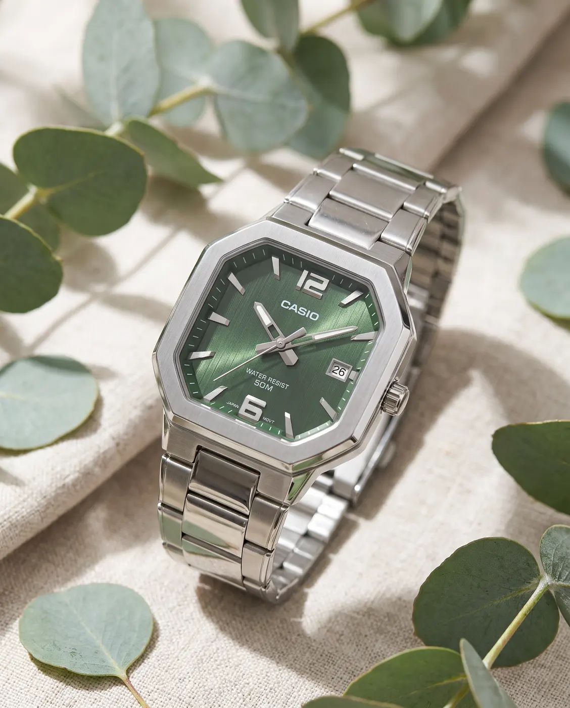 Đồng hồ Casio mặt xanh đặt trên vải linen với lá bạch đàn, ảnh sản phẩm dựng bằng AI